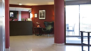 Un área de recepción con mostrador, cuadros enmarcados, una silla y vista a través de un vidrio.