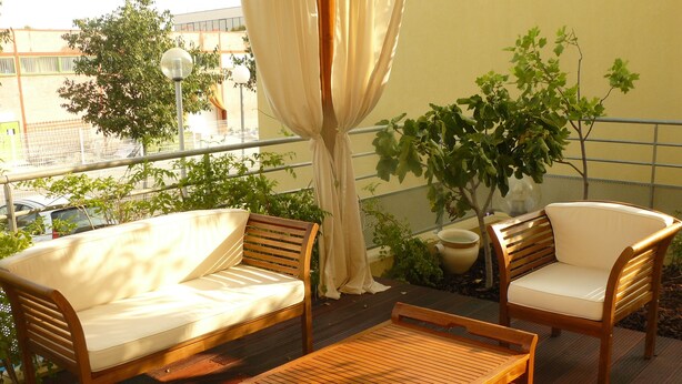 Una terraza de madera con un sofá y dos sillones, una mesita y una planta en maceta.