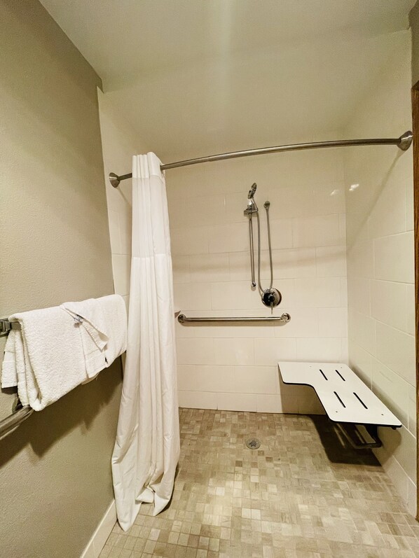 A shower area with a white tiled wall, a showerhead, a grab bar, and a towel rack with towels. - Sleep Inn & Suites Madison West (Madison)