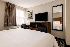 A hotel room with a large bed, a flat-screen TV, a desk with a computer, a refrigerator, and a mirror reflecting the bed.