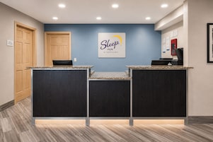 A reception desk with a sign for Sleep Inn by Choice Hotels, wooden doors, and a red fire alarm.