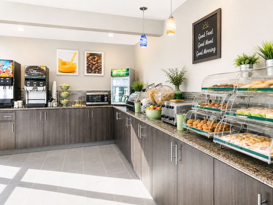 Angolo della colazione a buffet con macchine da caffè, un forno a microonde e diversi alimenti esposti in teche di vetro.