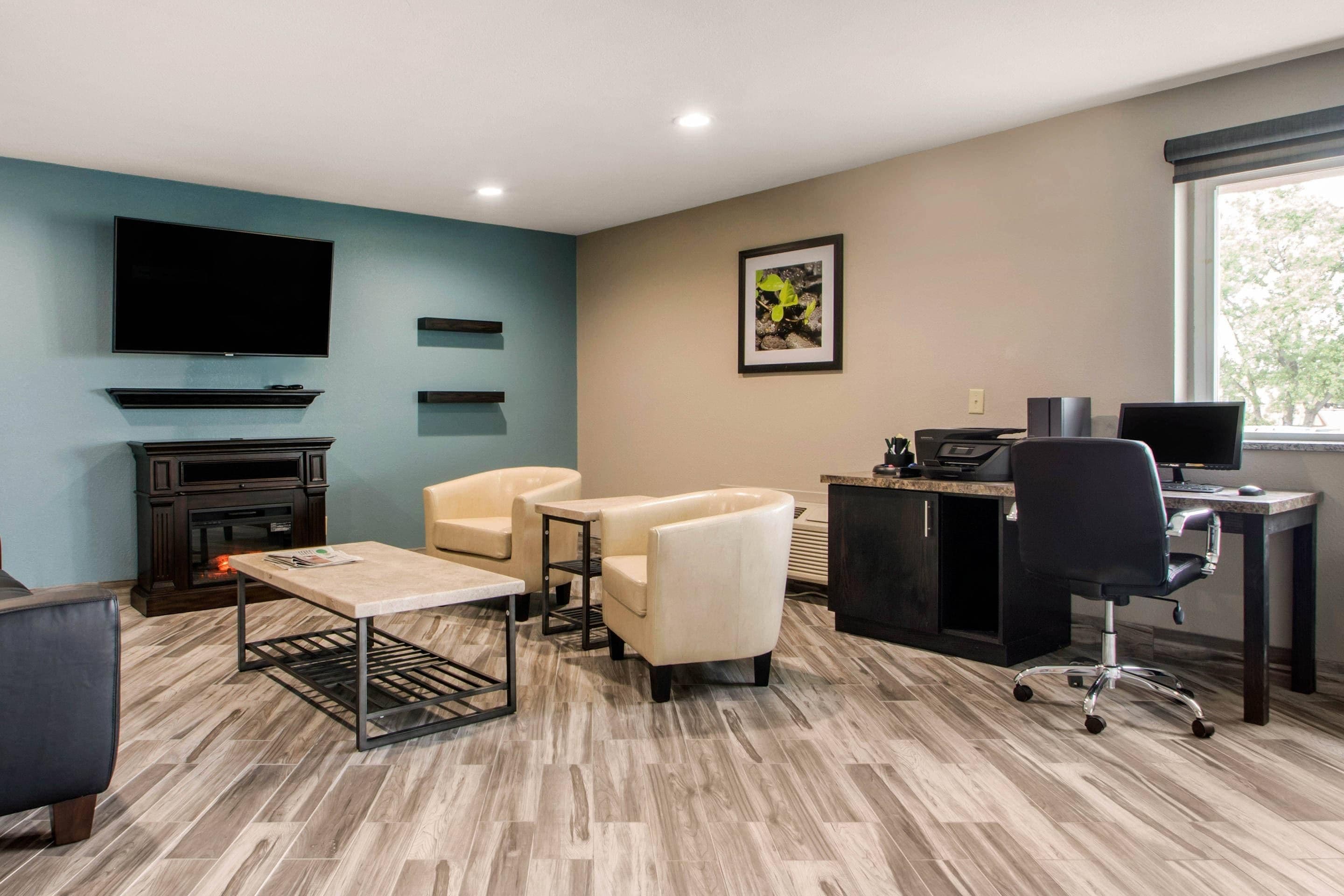 A modern living room with a fireplace, comfortable seating, a flat-screen TV, and a desk with a computer.