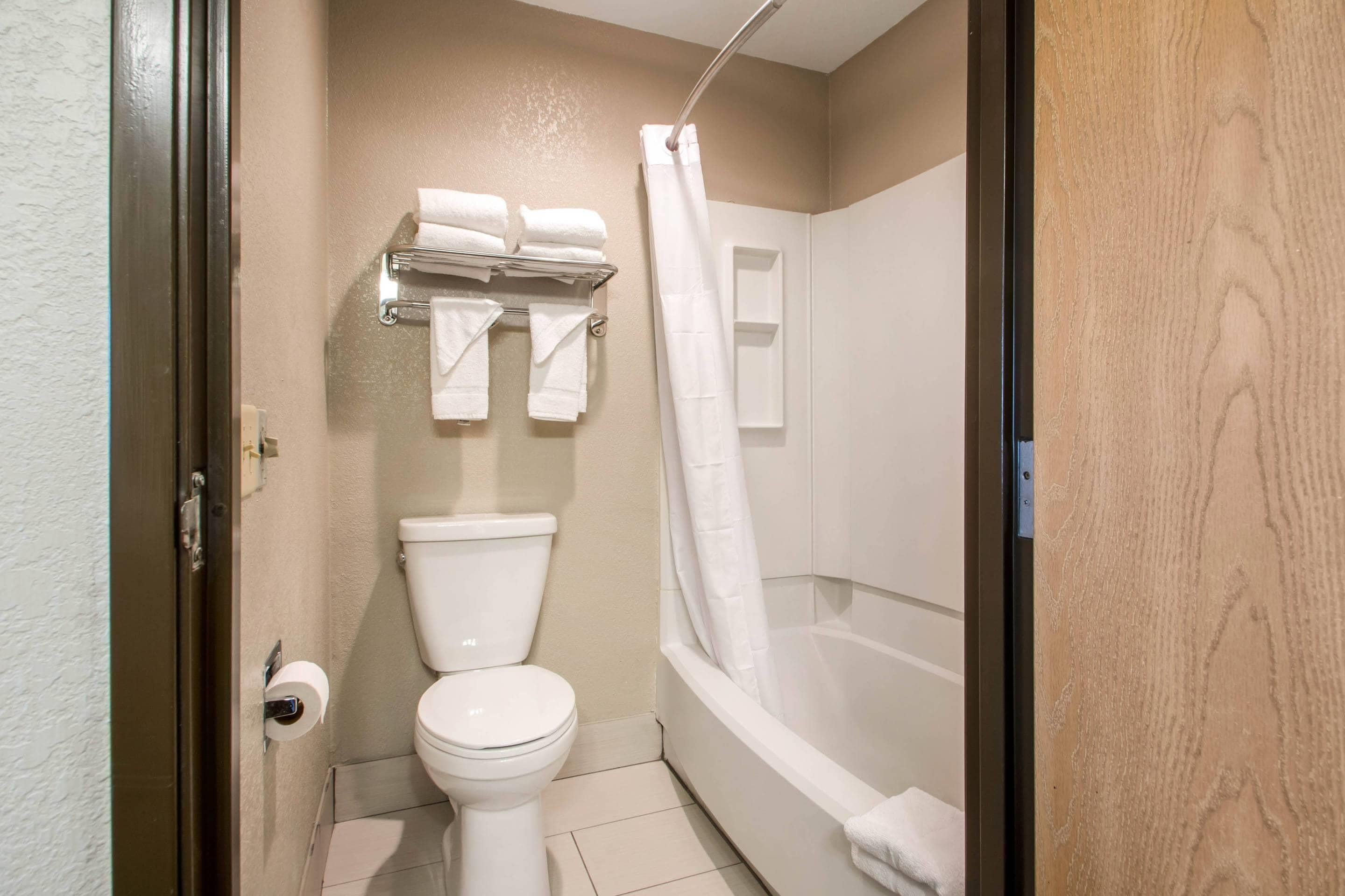A bathroom with a toilet, a shower with a curtain, and a towel rack with multiple towels.