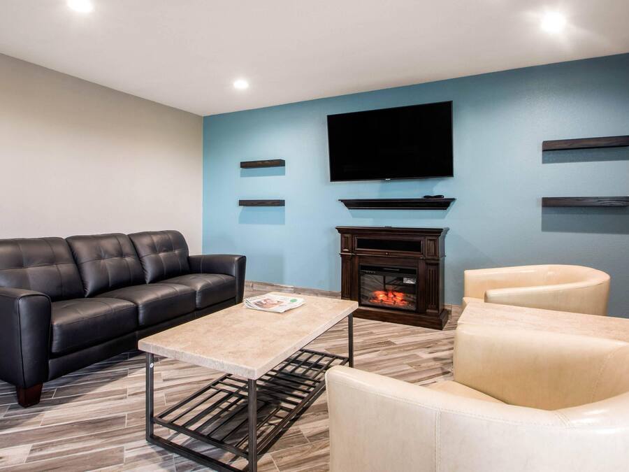 A modern living room with a black leather sofa, a beige armchair, a coffee table, a fireplace, and a flat-screen TV mounted on the wall.