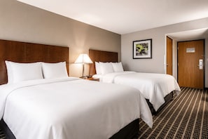 Ein Hotelzimmer mit zwei Betten, einem Nachttisch mit Lampe, einem gerahmten Bild an der Wand und einer Tür.