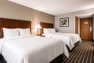 A hotel room with two beds, a nightstand with a lamp, a framed picture on the wall, and a door.