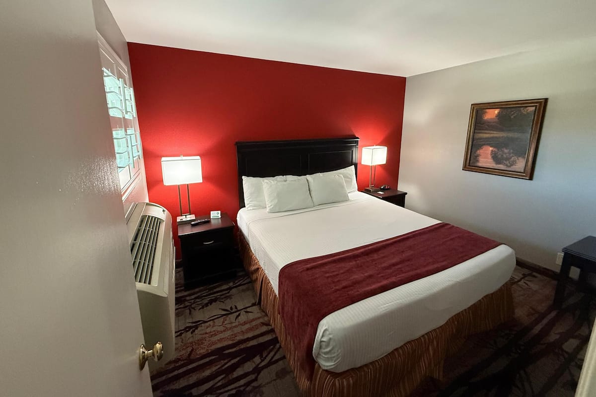 Ein Hotelzimmer mit einem großen Bett, zwei Nachttischen mit Lampen, einem Heizkörper, einer roten Wand und einem gerahmten Bild an der Wand.
