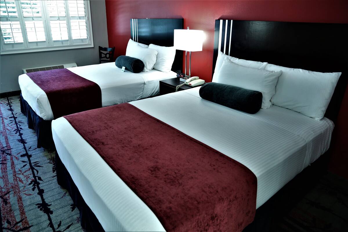 Ein Hotelzimmer mit zwei Betten, einem rot-weißen Farbschema, einem Nachttisch mit Lampe und einem Fenster mit Jalousien.