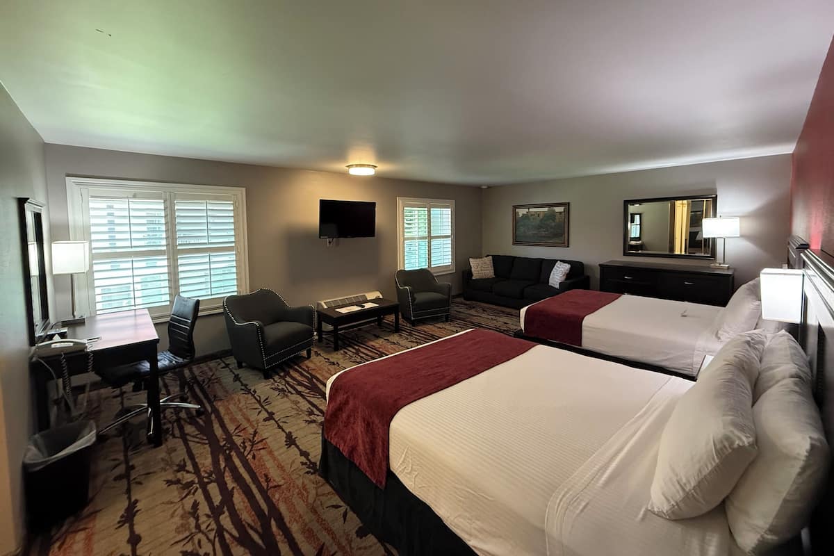 Ein Hotelzimmer mit zwei Betten, einem Schreibtisch, einem Sessel, einer Couch und einem Fernseher.