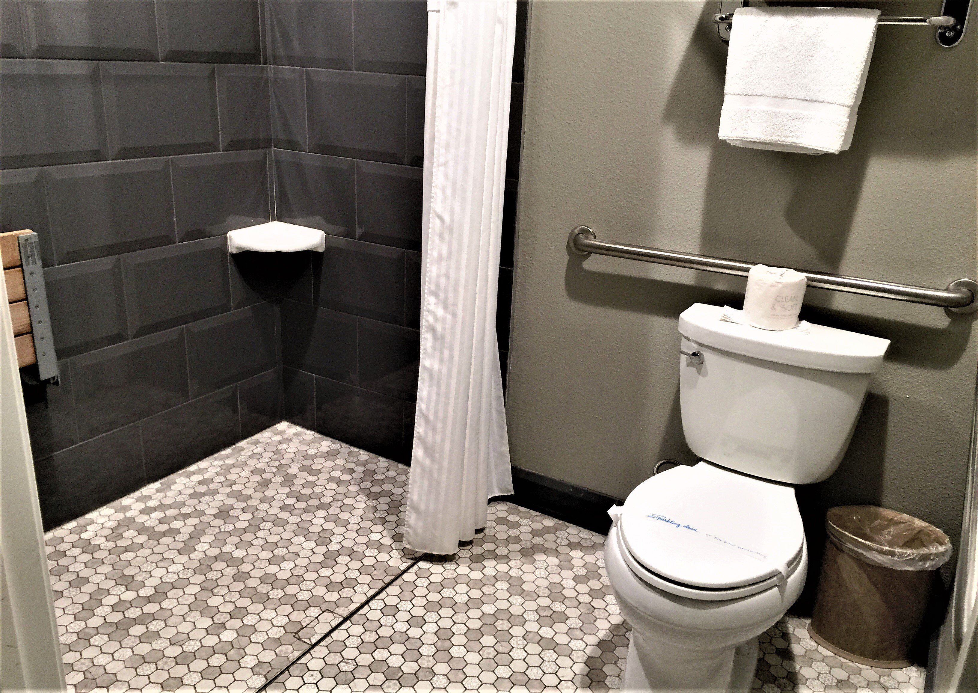 Een kleine, praktische badkamer met een wit toilet, een douchegordijn, een handdoekhouder en een prullenbak.