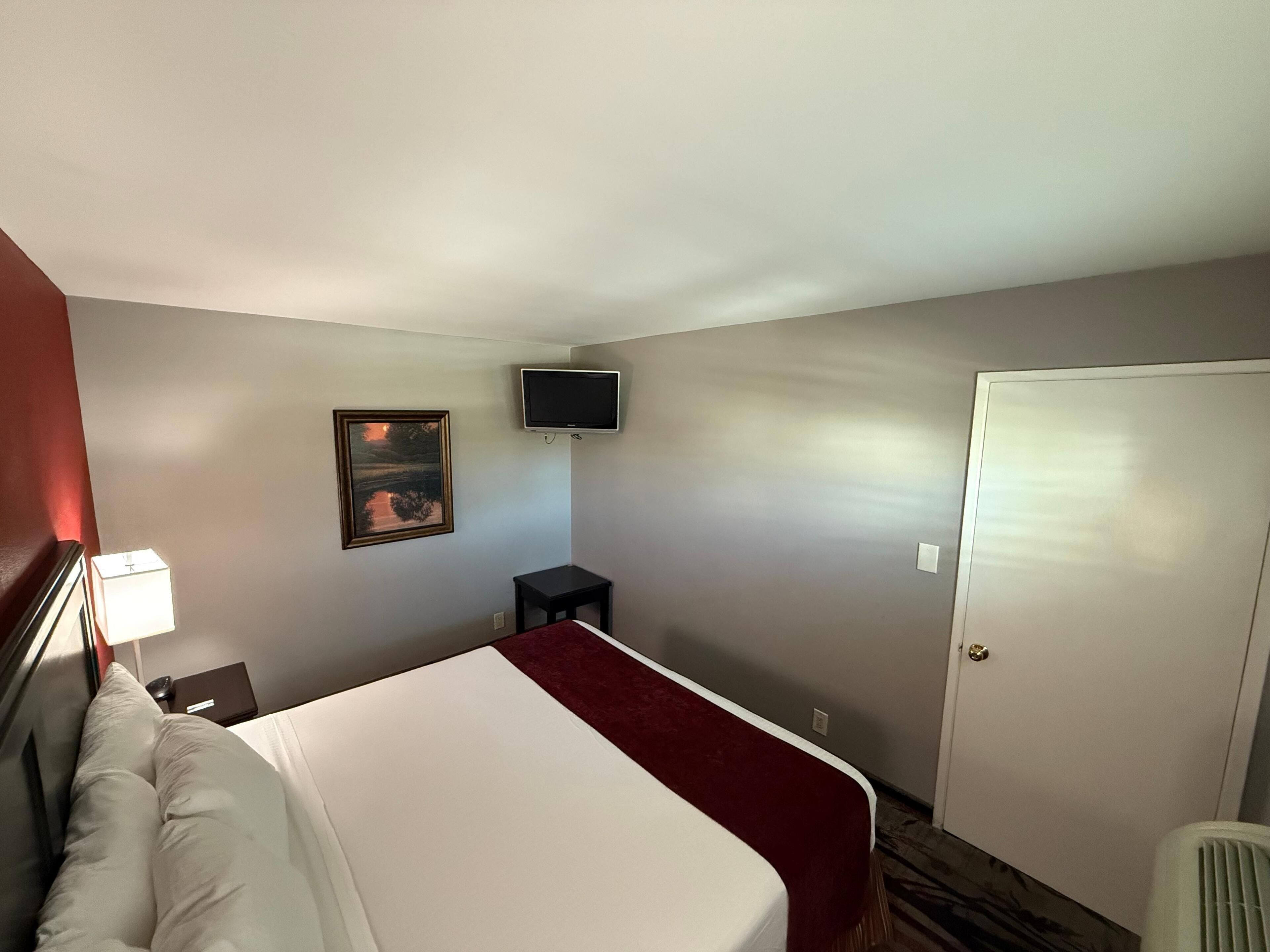 Une chambre d’hôtel avec un lit, un bureau, une chaise, une télévision et une porte.