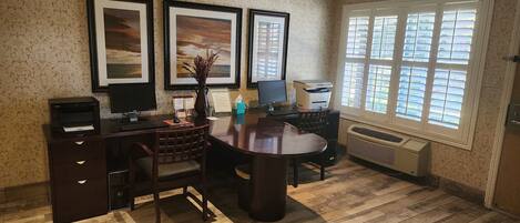 A well-lit office with a desk, chair, computer, printer, and framed artwork on the wall.