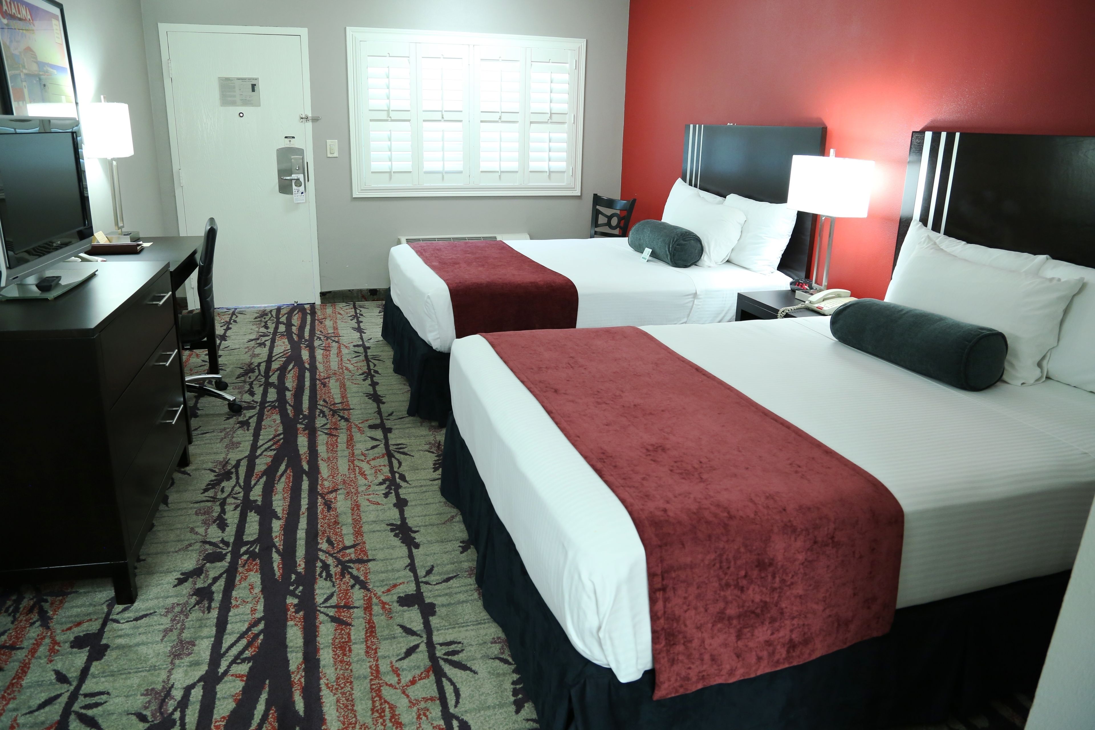 A hotel room with two beds, a desk with a computer, a chair, and a window with blinds.
