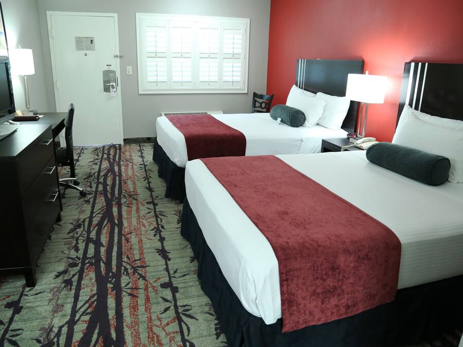 A hotel room with two beds, a desk with a computer, a chair, and a window with blinds.