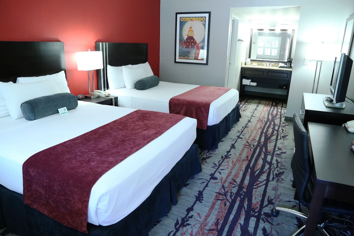 Ein Hotelzimmer mit zwei Betten, einem Schreibtisch, einem Stuhl, einem Fernseher und einem durchgegangenen Tür erkennbaren Badezimmer.