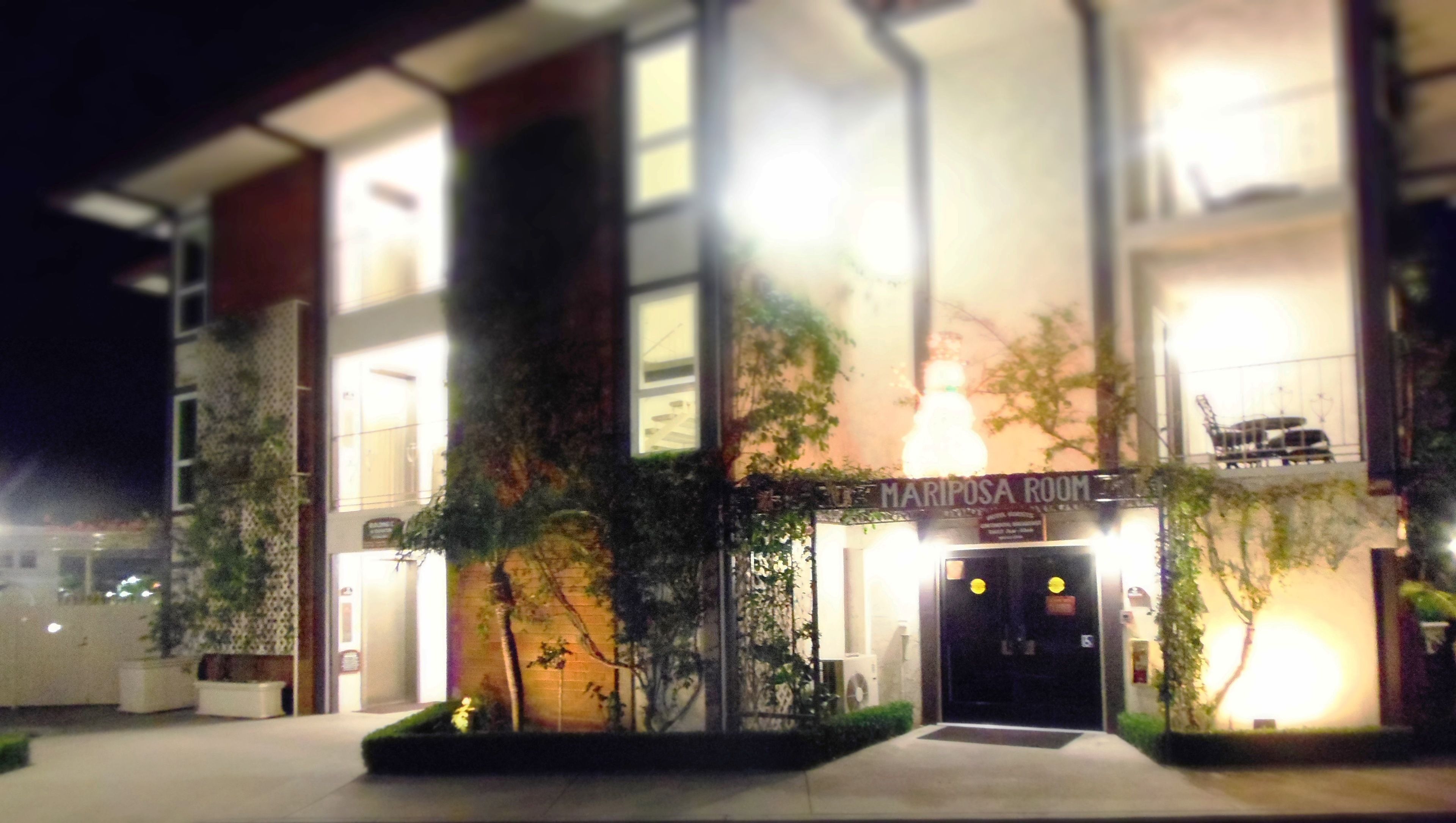 A building with a sign reading "MARIPOSA ROOM" at the entrance, surrounded by potted plants and a well-lit facade.