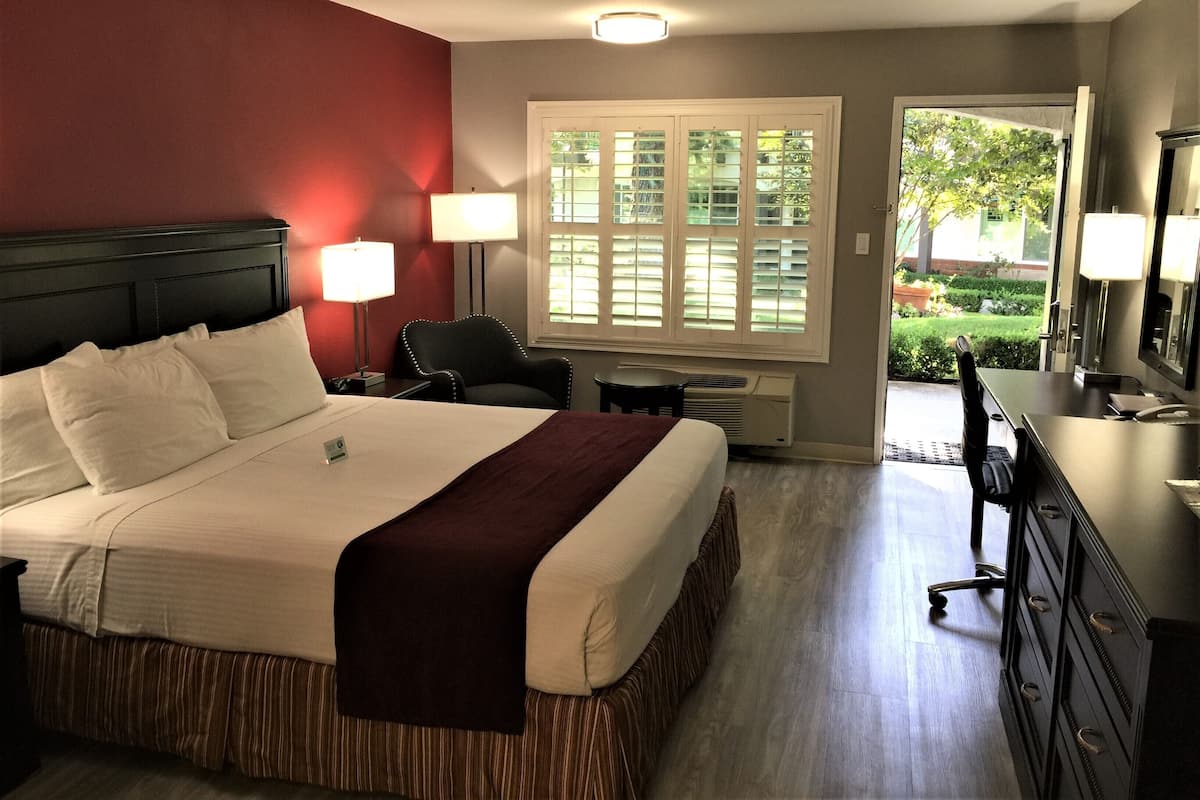 Ein Hotelzimmer mit einem großen Bett, zwei Nachttischlampen, einem Schreibtisch mit Stuhl, einem Schminktisch und einem Fenster mit Jalousien.