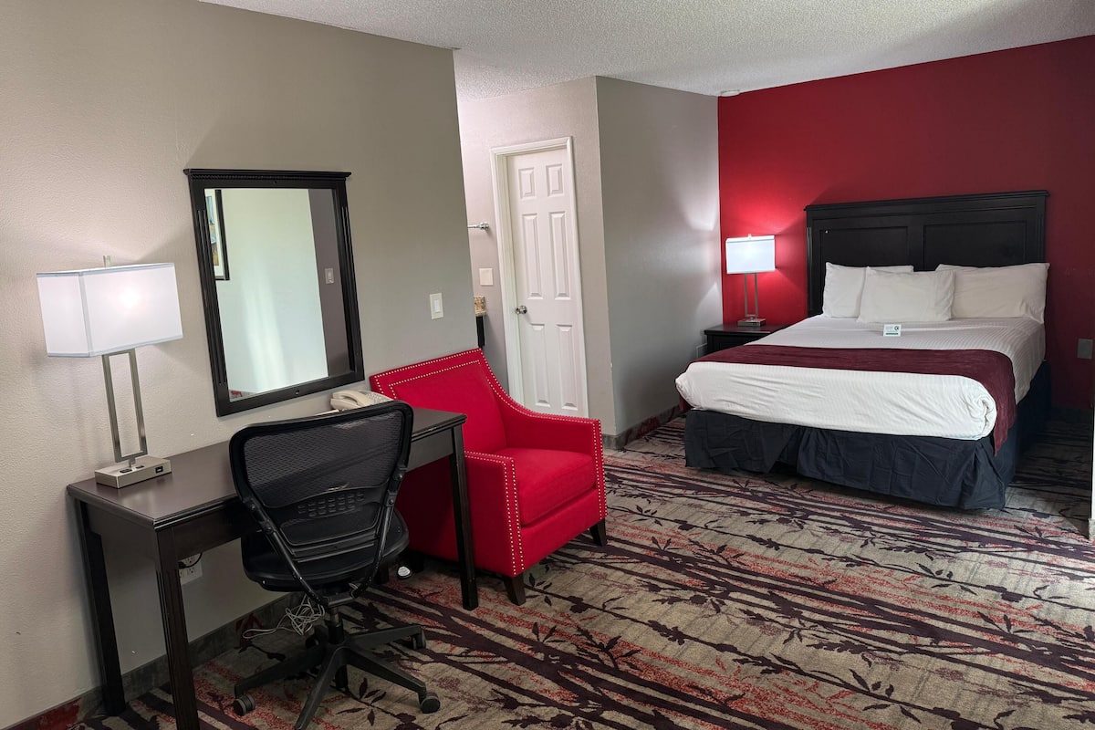 Ein Hotelzimmer mit Schreibtisch, Stuhl, Bett und einer roten Akzentwand.
