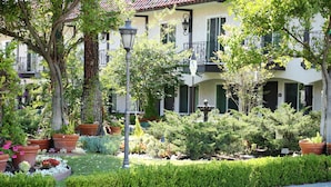 A building with a tiled roof, multiple balconies, and a well-maintained garden with various plants and a fountain.