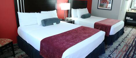 Une chambre d’hôtel avec deux lits, un mur rouge, un tableau encadré, une table de chevet et une moquette à motifs.