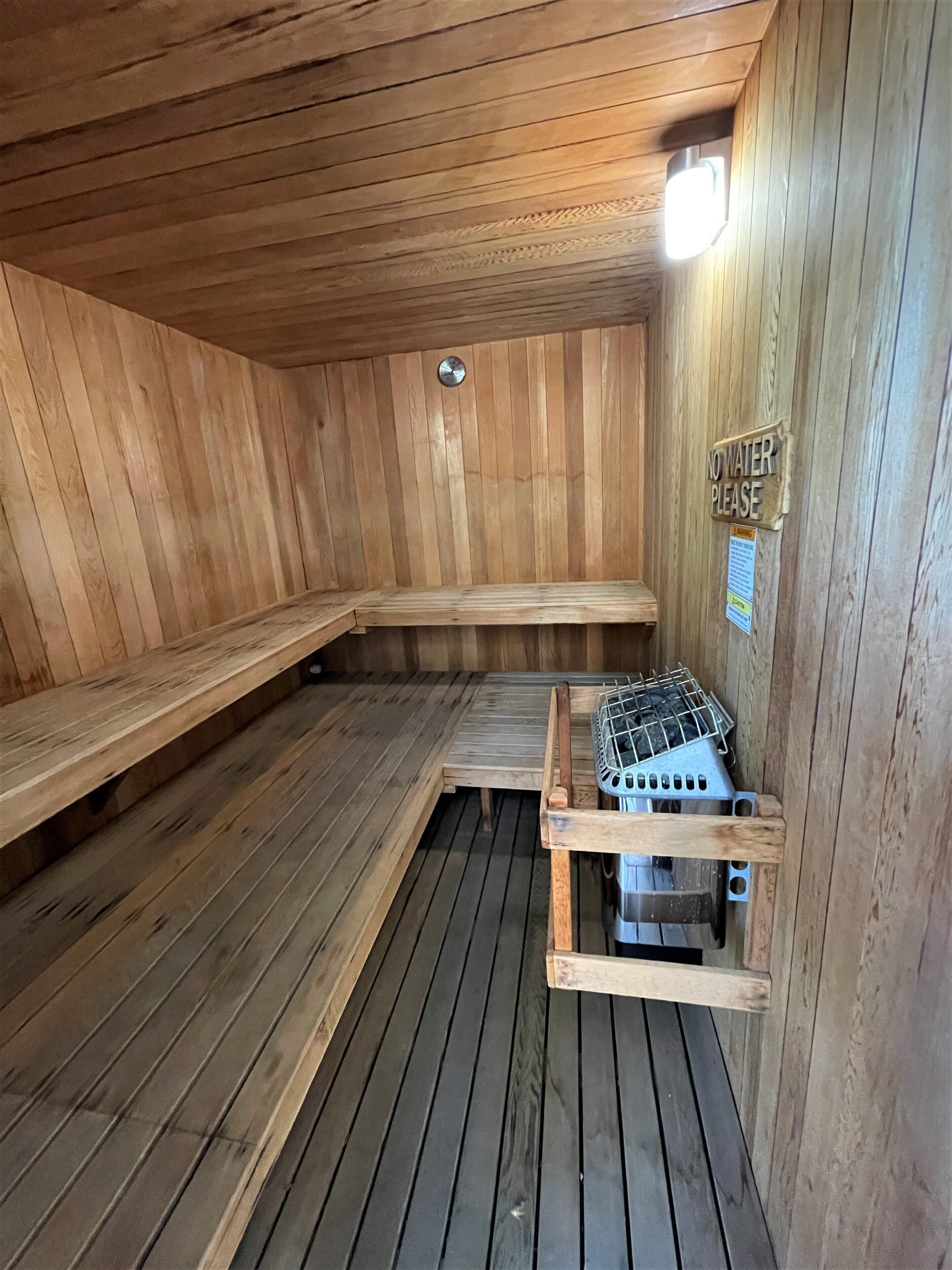 Una sauna con paredes y bancos de madera, un calentador de metal y un letrero que dice 'No Water Please'.