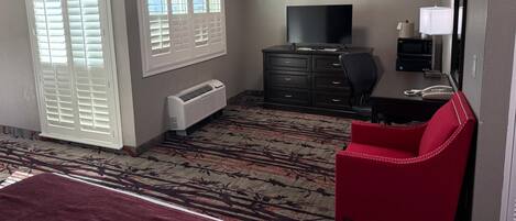 Una habitación de hotel con una cama, una silla roja, un televisor, un escritorio con lámpara y un microondas.