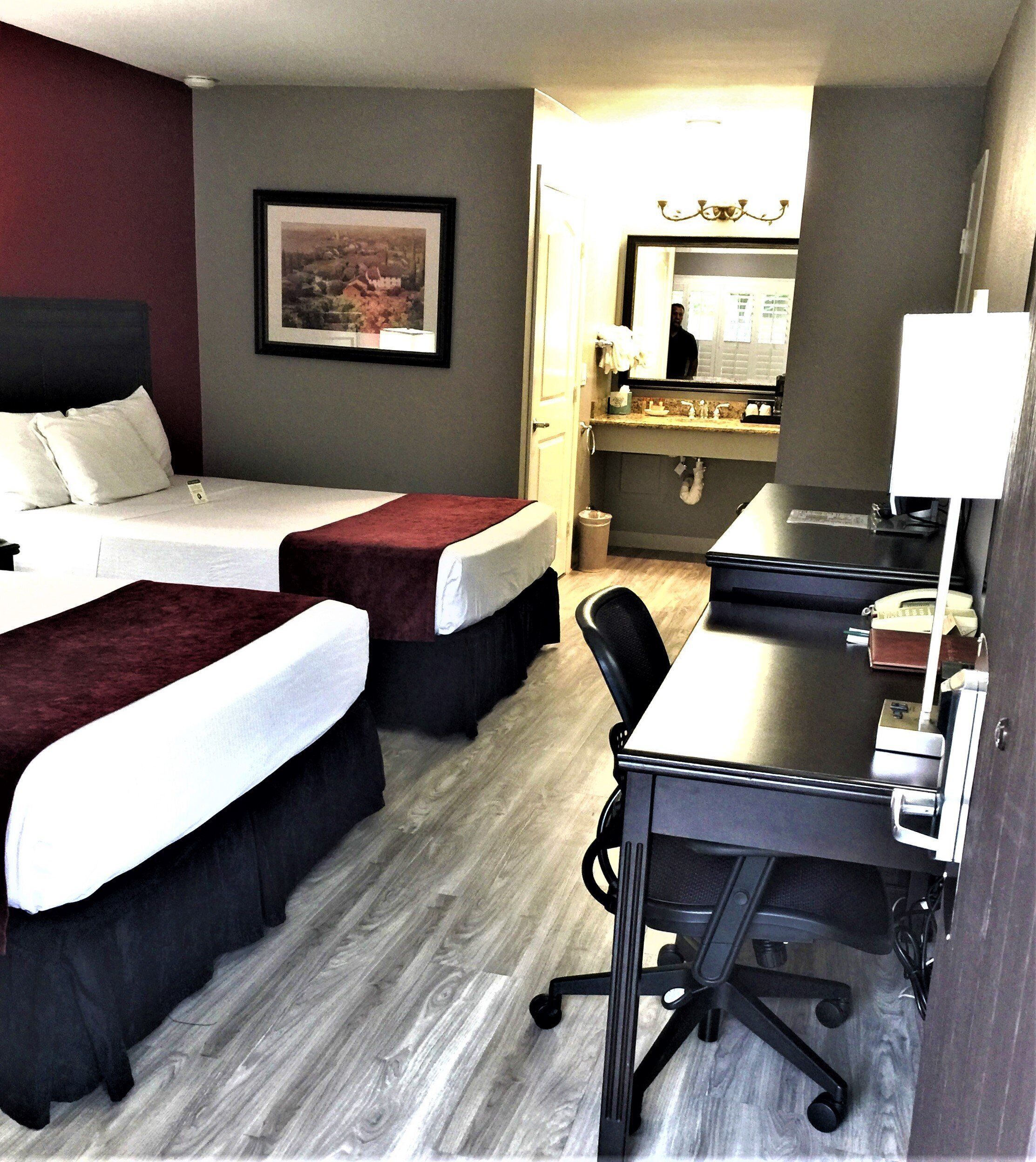 A hotel room with two beds, a desk, a chair, a mirror, and a picture on the wall.