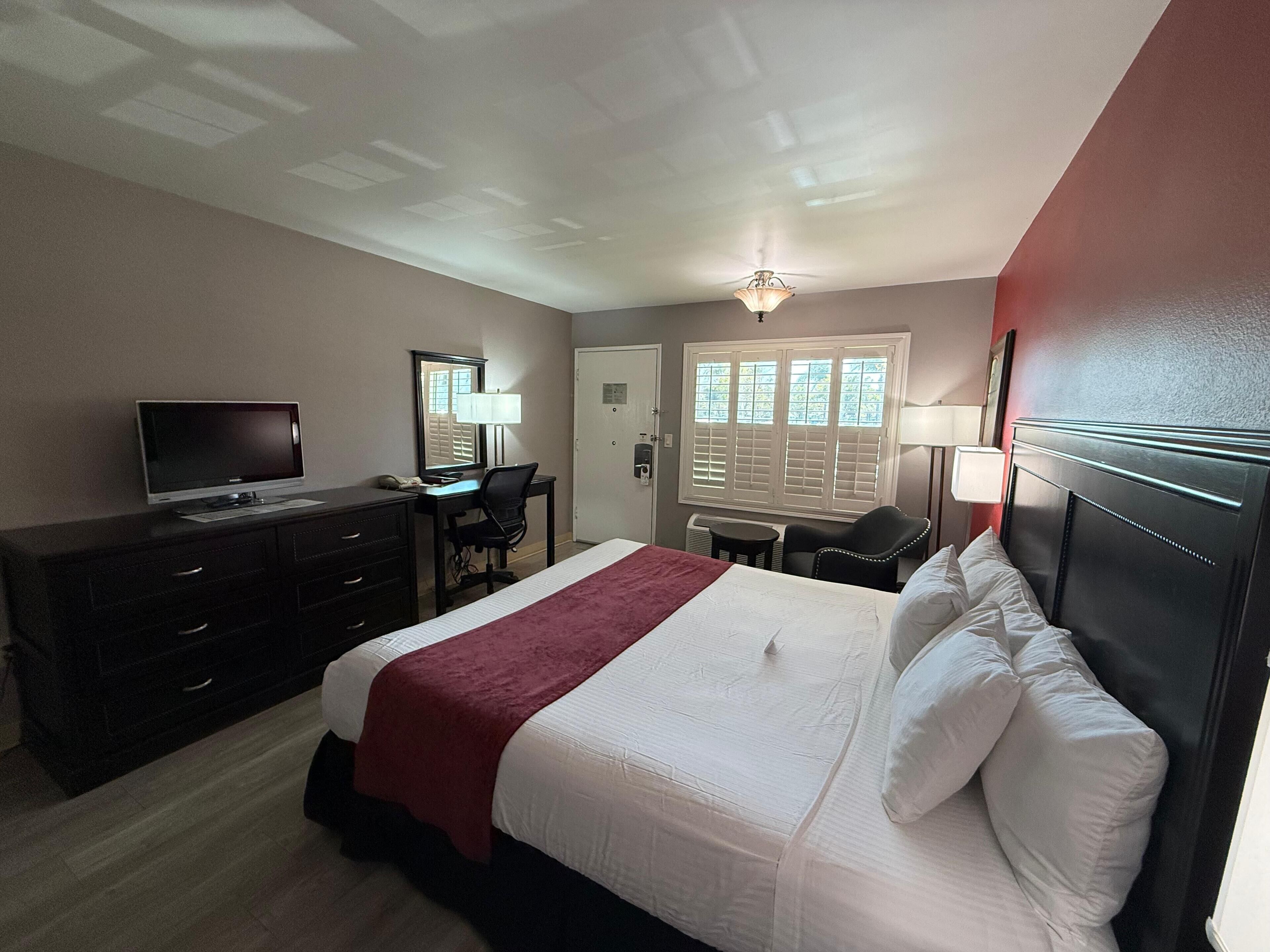 Una habitación de hotel con cama, escritorio, televisión y ventana con persianas.