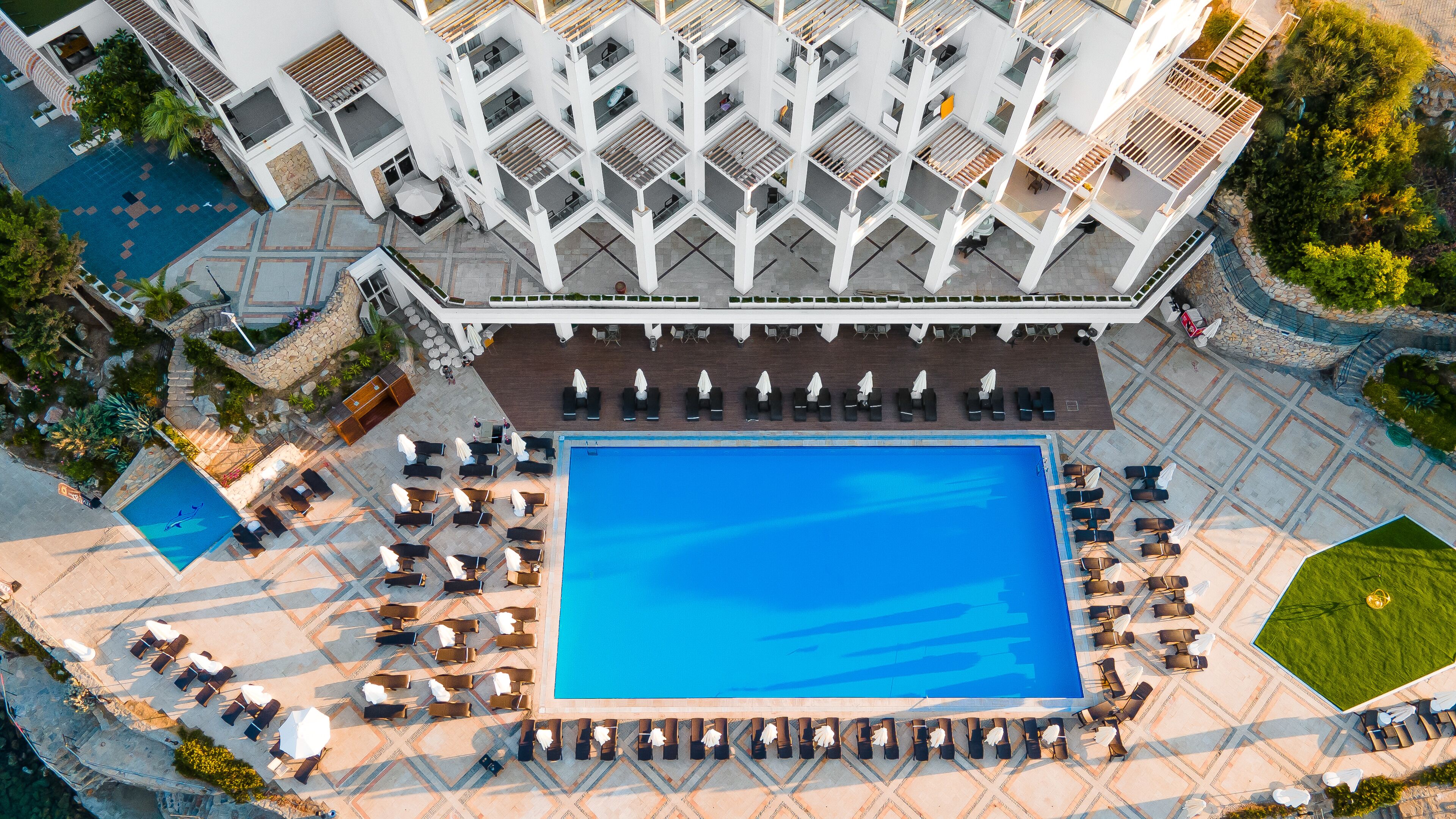 An aerial view of a hotel with a central swimming pool surrounded by sun loungers and a covered seating area.