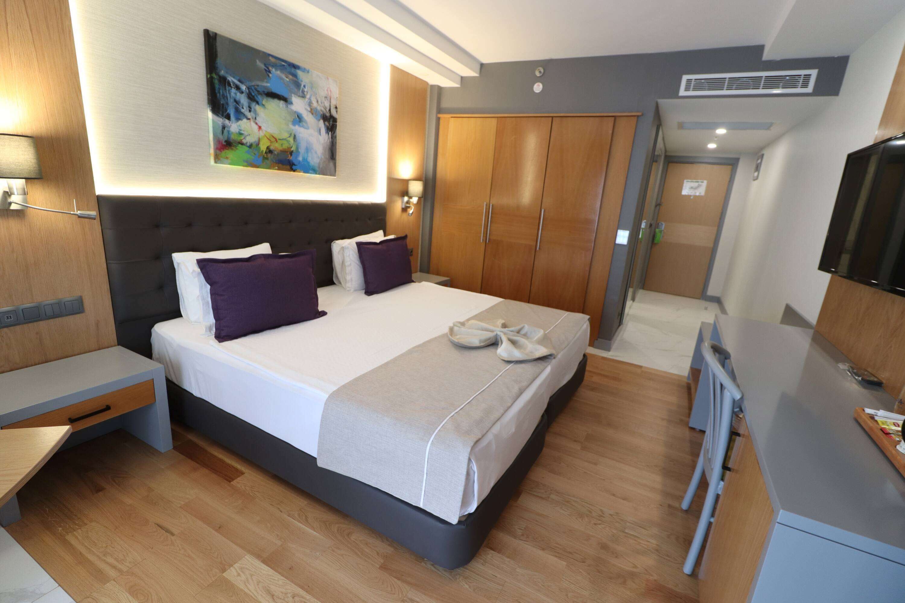 A modern hotel room with a large bed, wooden wardrobe, and a television.