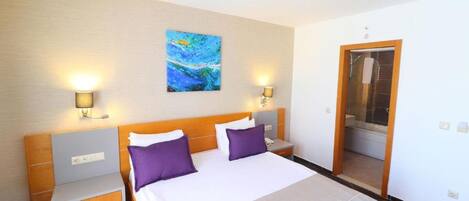 A hotel room with a large bed, two nightstands, a painting on the wall, and a bathroom door visible through an open doorway.