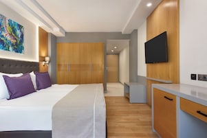 A modern hotel room with a large bed, a wardrobe, a desk, and a TV mounted on the wall.