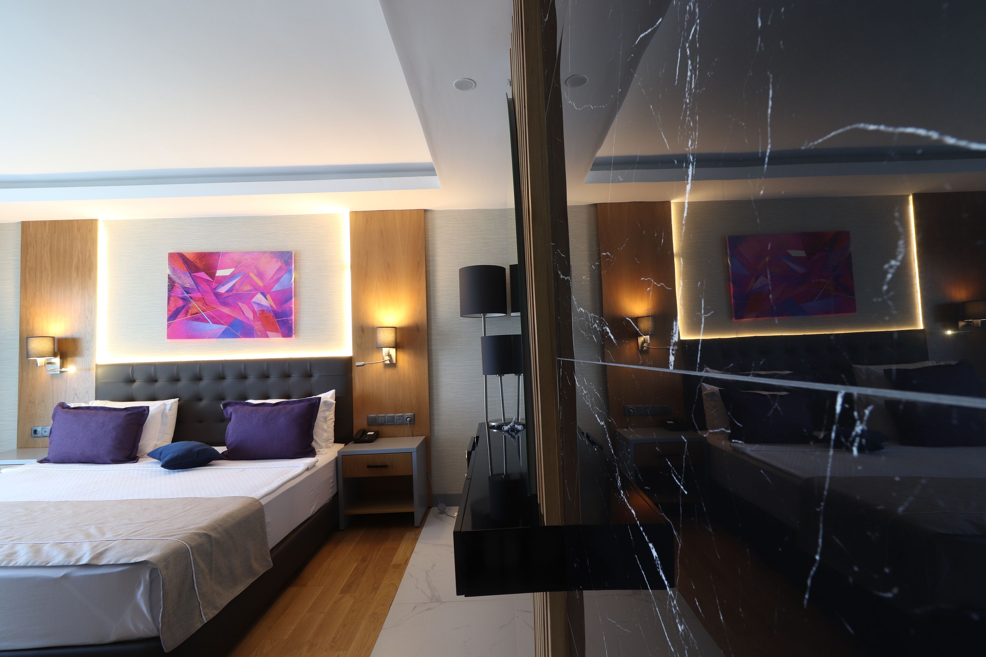 Ett modernt hotellrum med en stor säng, ett nattduksbord, en TV och konstverk på väggarna.