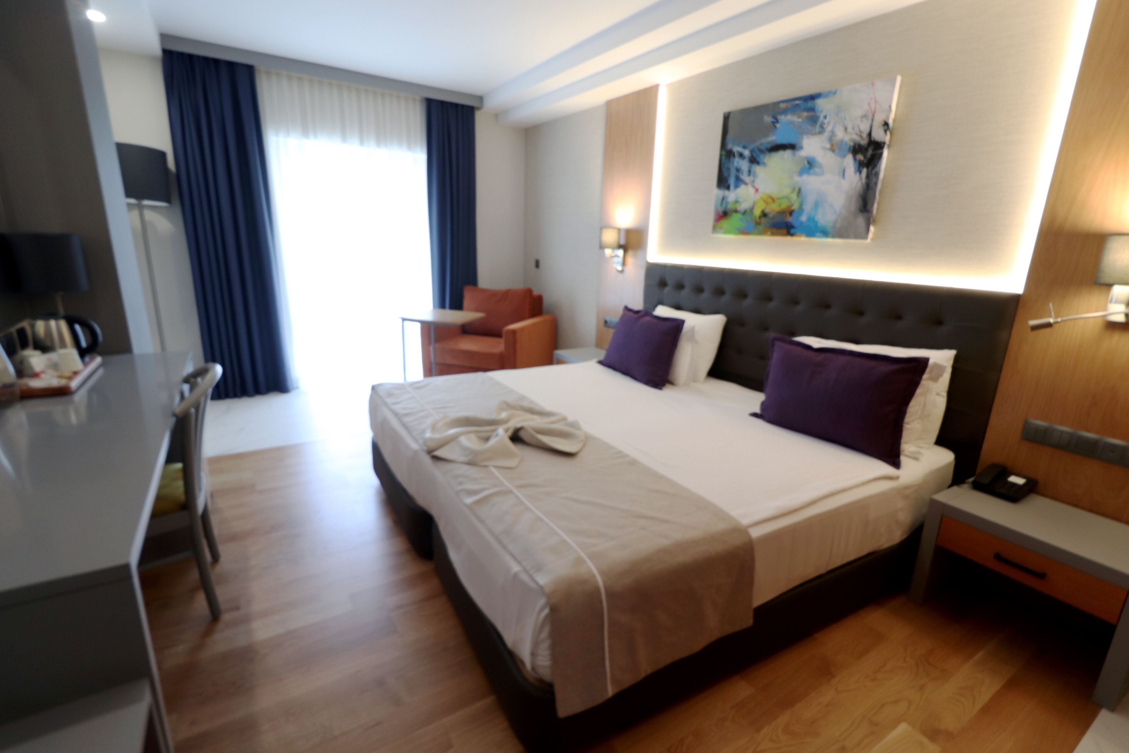 Quarto de hotel com uma cama grande, uma mesa de escritório, uma cadeira, uma mesinha e um quadro na parede.