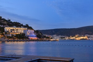 Un hôtel situé au bord de l’eau, doté de nombreux balcons, d’un quai et offrant une vue sur une ville historique de l’autre côté.