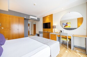 Habitación de hotel con una cama grande, un escritorio, una silla, un televisor y un espejo redondo.