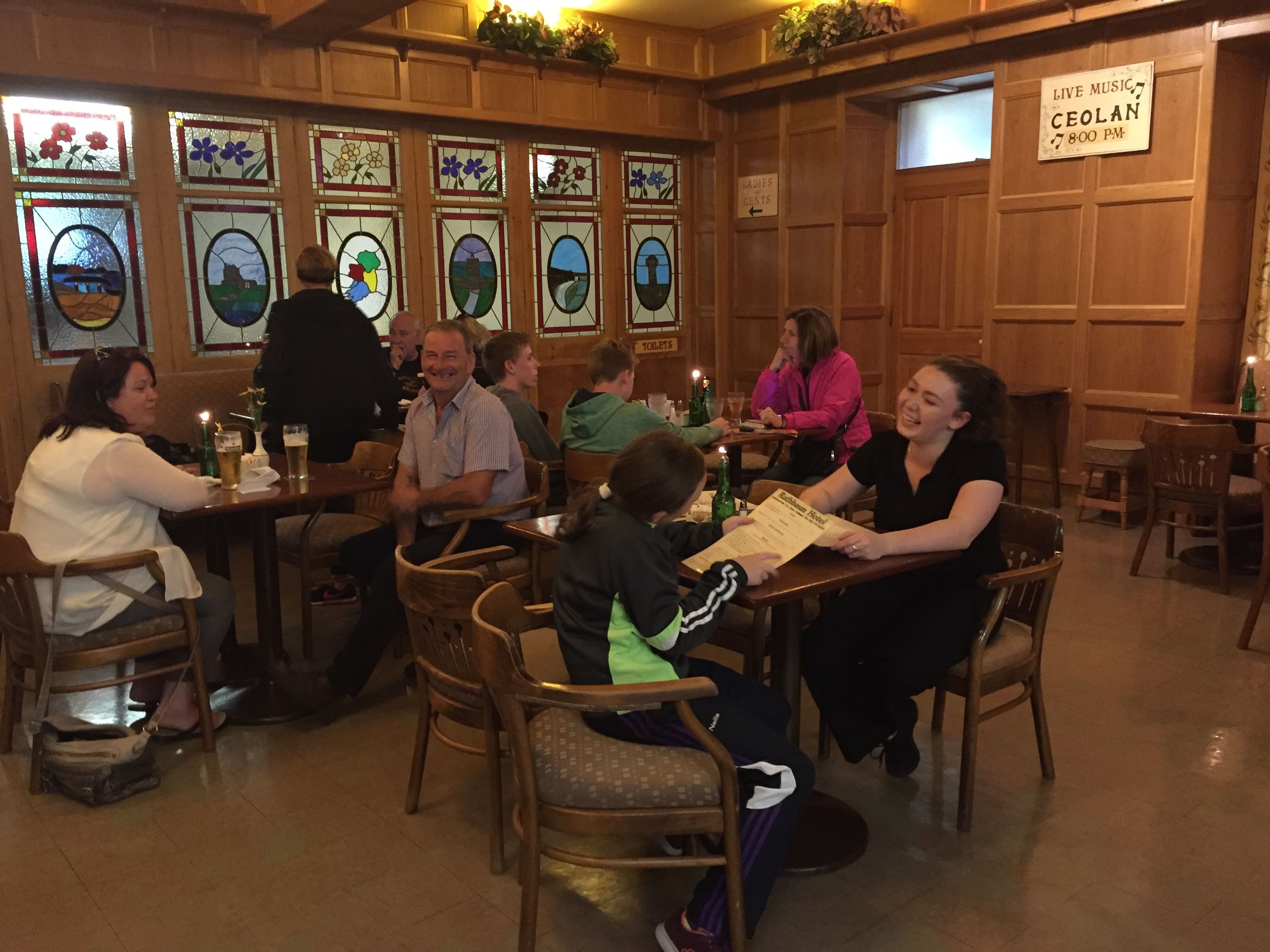 Interior de restaurante con paredes de paneles de madera, ventanas de vitral y un cartel que anuncia música en vivo a las 7:00 PM.