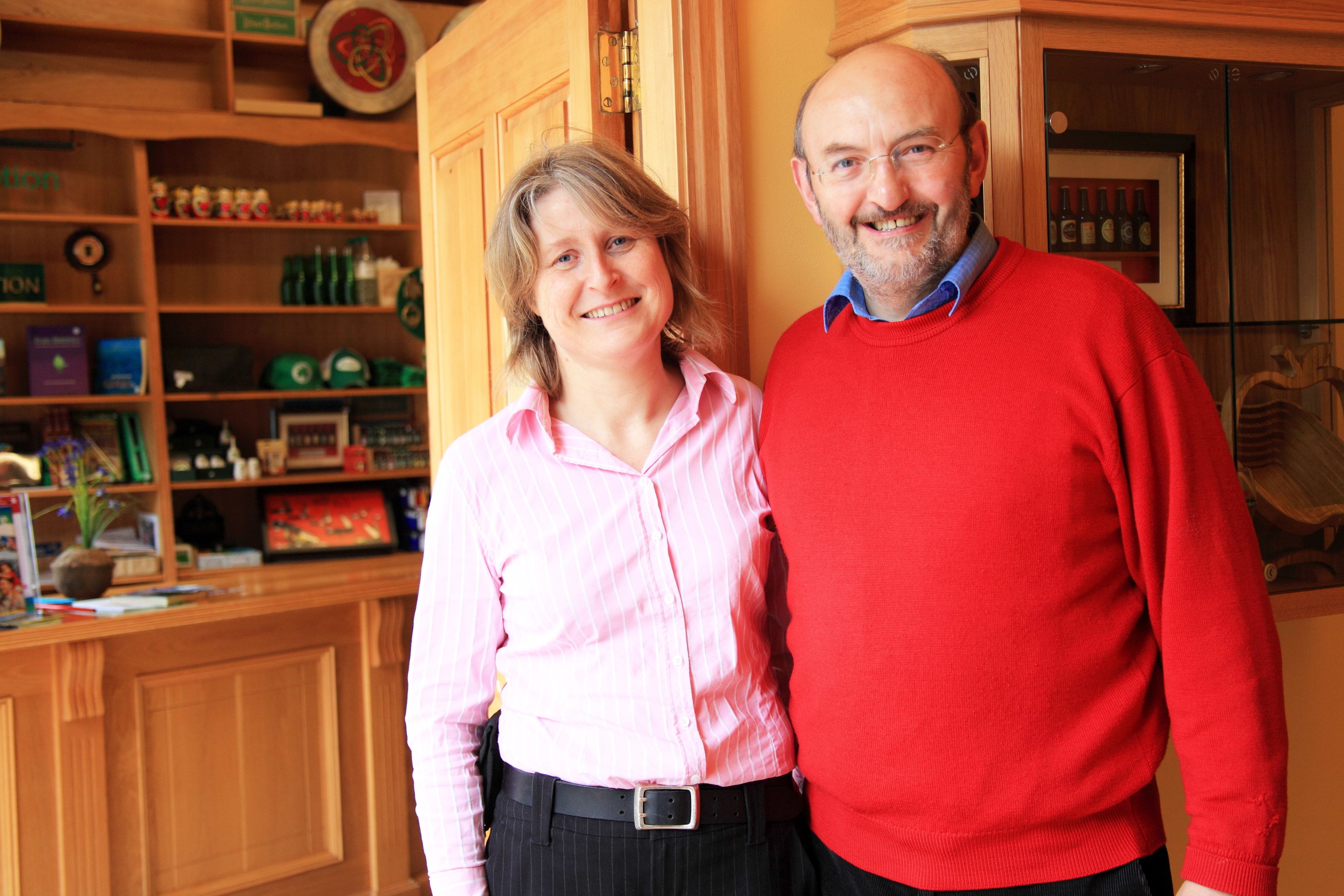 A man and a woman standing in a kitchen with wooden cabinets and various kitchen items.