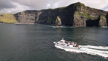 A boat with passengers, sailing near cliffs with a rocky coastline.