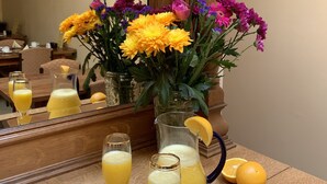 A wooden table with a vase of flowers, a pitcher of orange juice, and glasses of orange juice. - Rathbaun Hotel (Lisdoonvarna)