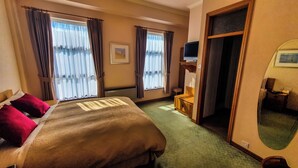 A hotel room with a bed, two windows with curtains, a television, a small table, and a mirror.