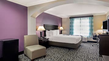 A hotel room with a large bed, two bedside tables with lamps, a chair, a desk with a computer, and a TV.