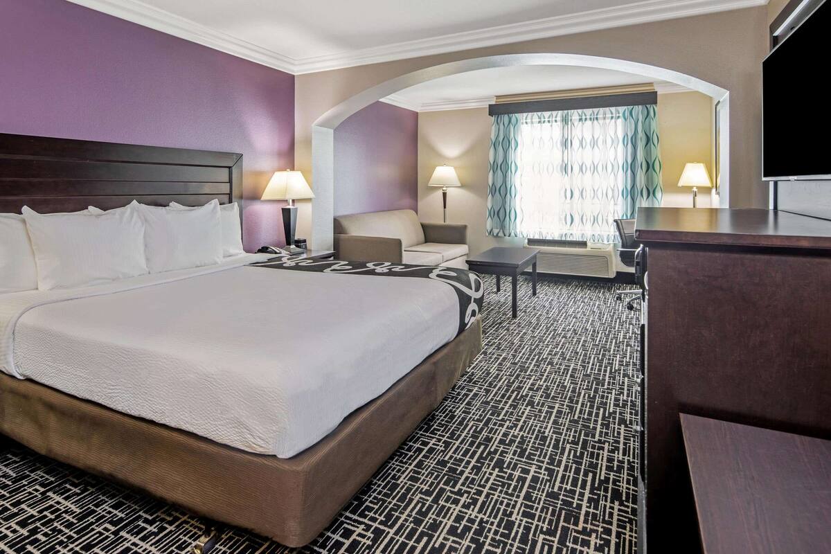 A hotel room with a large bed, a desk, a chair, and a TV.