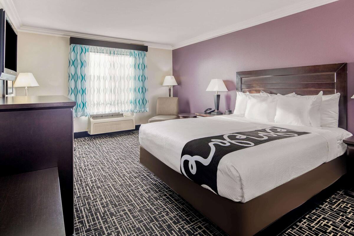 A hotel room with a large bed, two bedside tables with lamps, a desk, and a window with curtains.