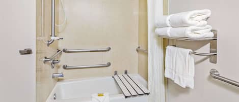 A bathroom with a bathtub, grab bars, a shower, and a towel rack with folded towels.
