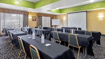 Un salón de conferencias con varias mesas y sillas, una pizarra y una pantalla de proyector.