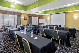 Un salón de conferencias con varias mesas y sillas, una pizarra y una pantalla de proyector.