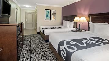 Habitación de hotel con dos camas, televisión, escritorio con lámpara y alfombra estampada.