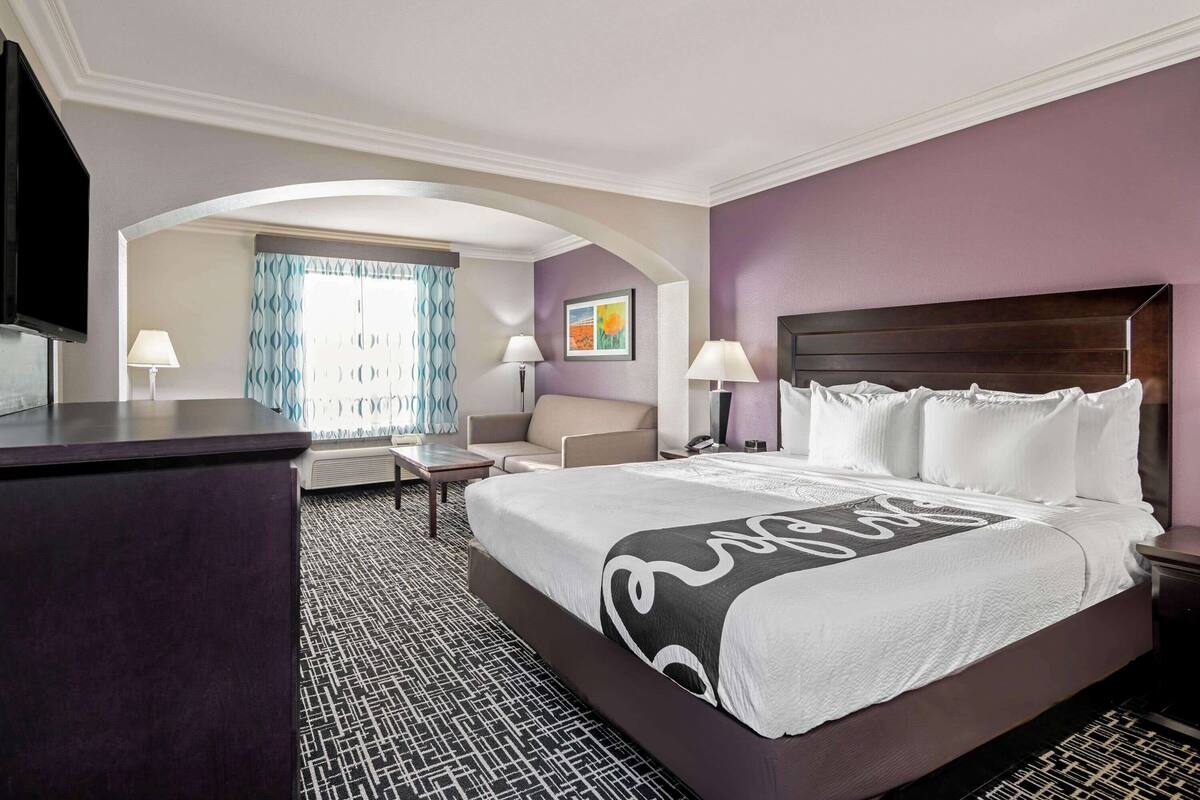 A hotel room with a large bed, a desk, a chair, and a television.